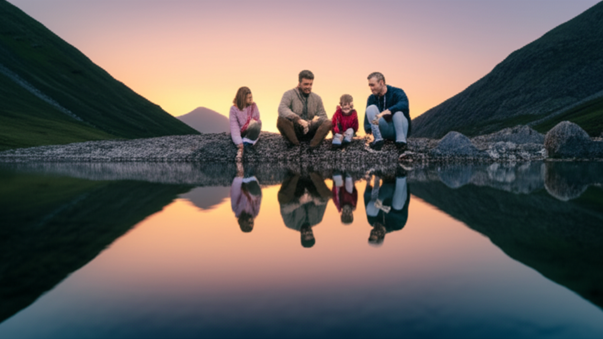 A peaceful scene of a family sitting by a crystal clear mountain stream at dusk. The water reflects 
