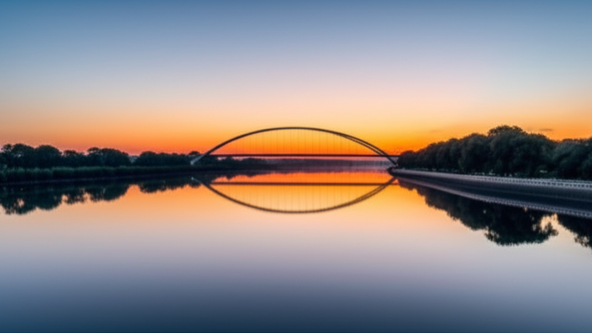 A serene landscape showing a calm river reflecting the soft colors of a sunrise. In the distance, a 