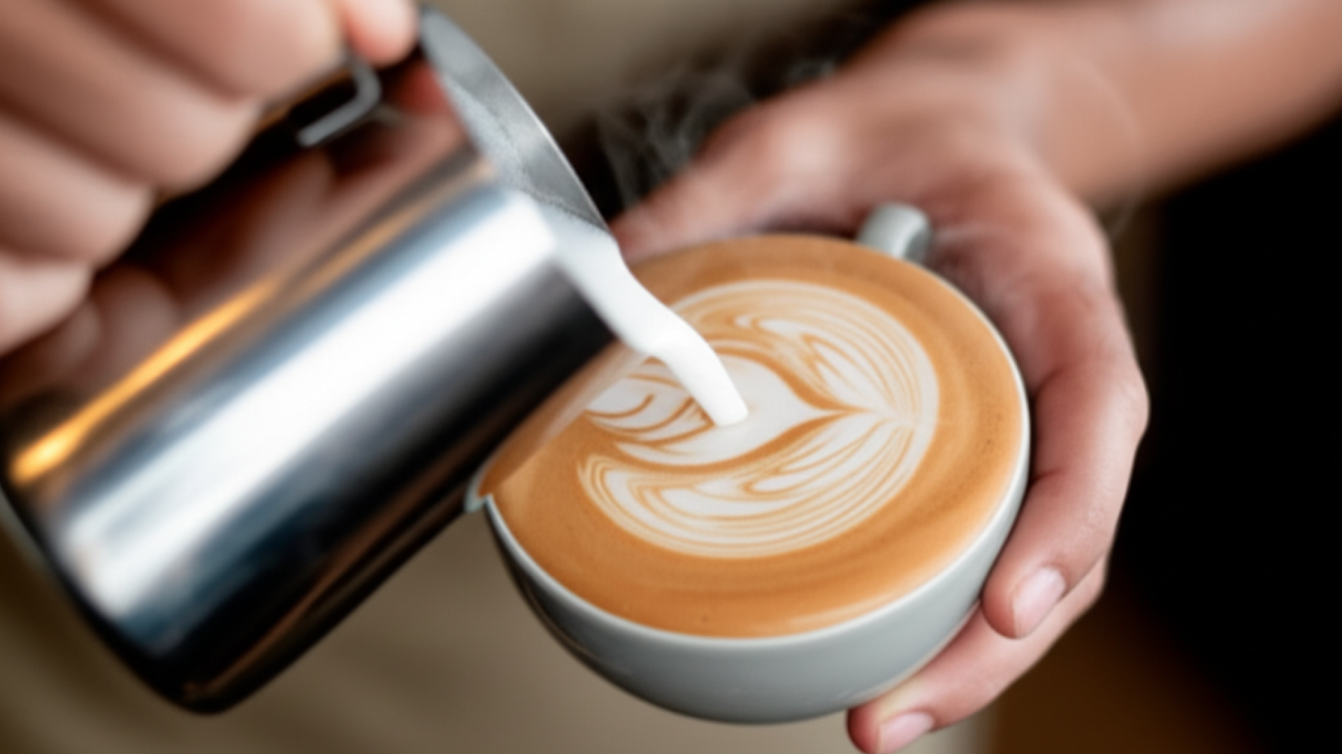 Close-up of a barista's hands pouring creamy oat milk into a ceramic cup of espresso, creating beaut